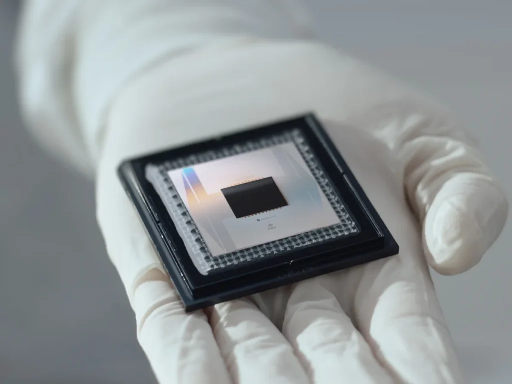 Dłoń naukowca w białej rękawiczce trzymająca procesor kwantowy Google Willow – czarny, kwadratowy układ krzemowy na ceramicznej obudowie ze srebrnymi stykami.